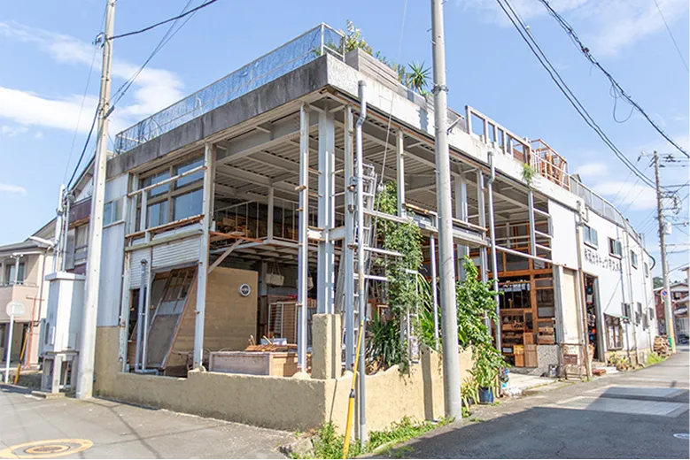 晴れた日の街角に立つ、鉄骨の骨組みが見える2階建ての建物。屋上にはフェンスが設置されている。