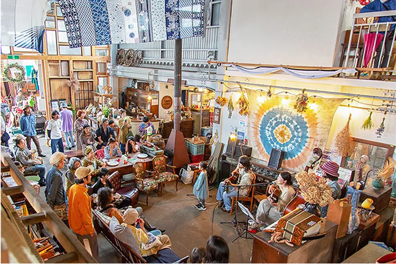 広い建物の中で多くの人が集まり、音楽の生演奏を聴いている。少し高い場所から見下ろした写真。