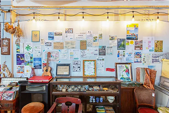 白い壁一面にたくさんのチラシや写真が貼られている。その前にはガラスケースと椅子が置かれている。