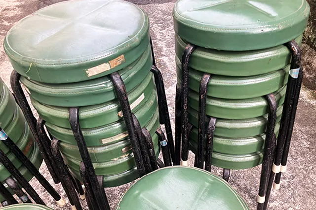 緑色のビニール張りの丸椅子が、いくつもの山になって積み重ねられている様子。