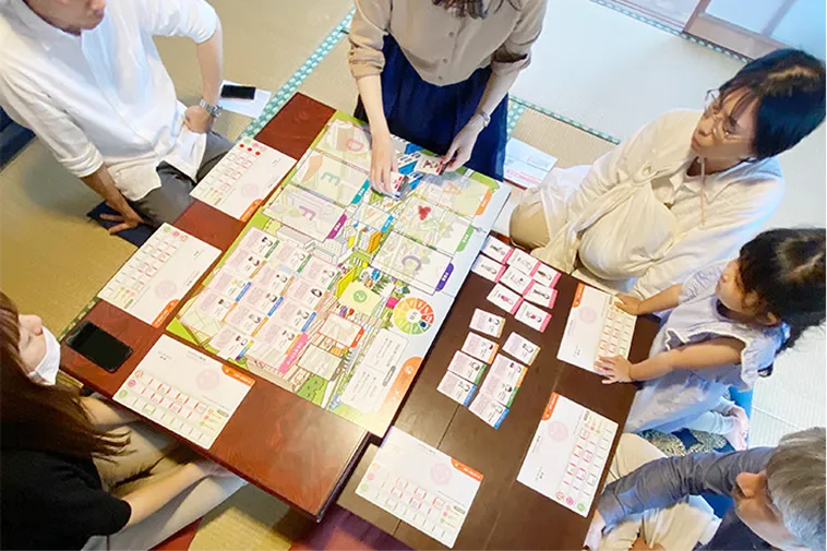 和室のテーブルで、大人と子供が一緒にボードゲームをしています。皆でゲーム盤をのぞきこんでいます。